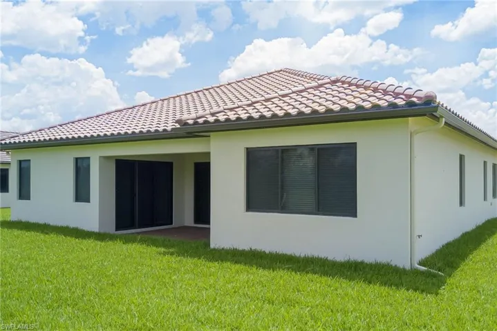 Back of property with stucco siding, a tiled roof, and a lawn