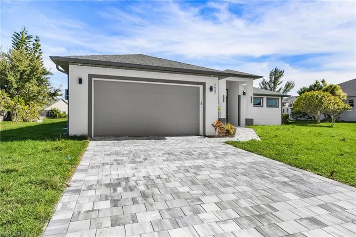 Prairie-style home with a front lawn, decorative driveway, a garage, and stucco siding
