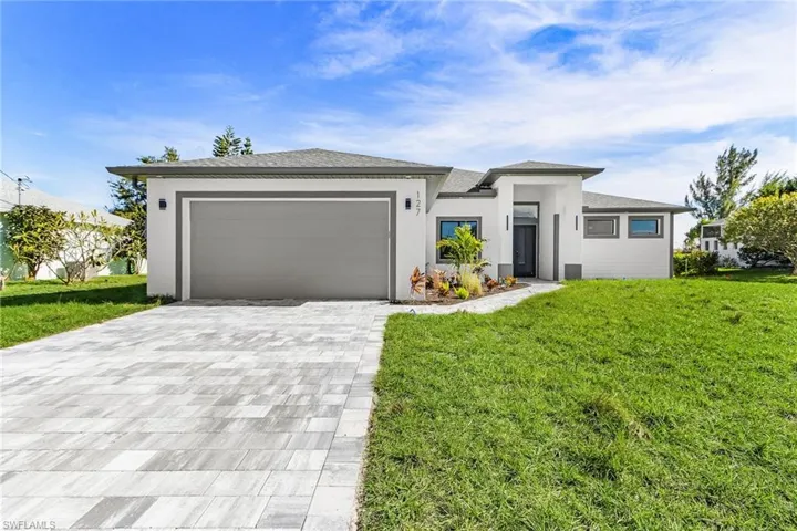 Prairie-style home featuring a front yard, decorative driveway, stucco siding, and a garage