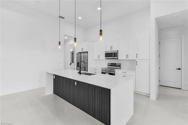 Kitchen with appliances with stainless steel finishes, decorative light fixtures, an island with sink, white cabinets, and light stone counters