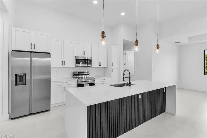 Kitchen with appliances with stainless steel finishes, light stone countertops, pendant lighting, white cabinetry, and an island with sink