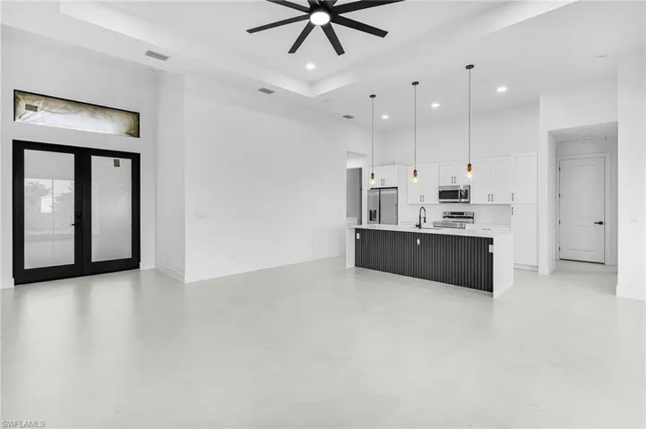 Kitchen with a high ceiling, open floor plan, pendant lighting, a large island, and white cabinetry
