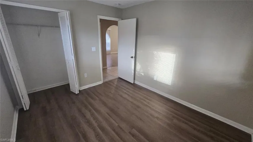 Unfurnished bedroom with arched walkways, dark wood-style flooring, and a closet