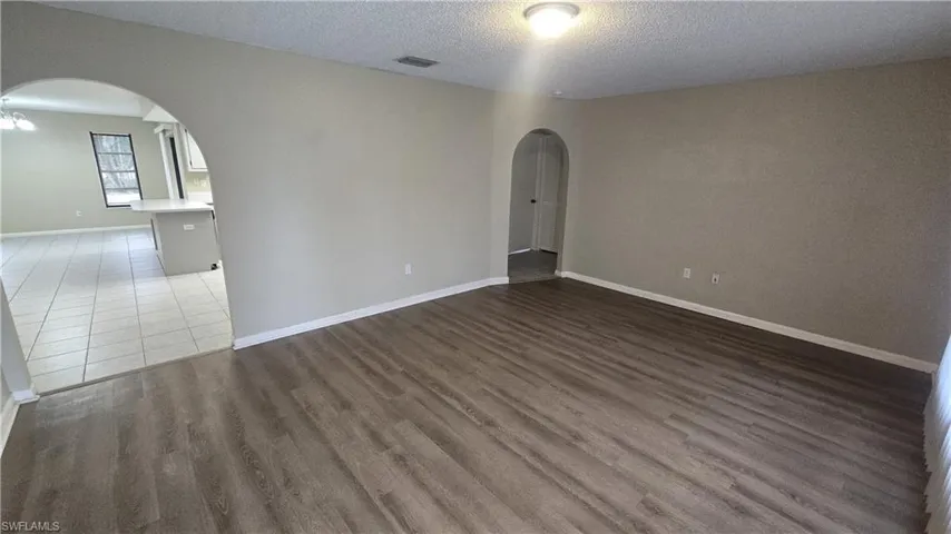 Empty room with arched walkways, a textured ceiling, and light wood-type flooring