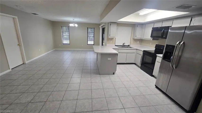 Kitchen featuring black appliances, light countertops, open floor plan, a chandelier, and white cabinets