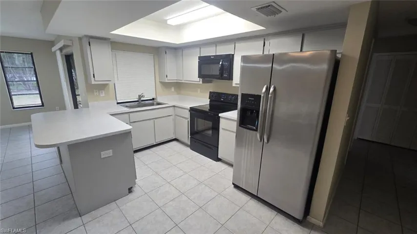 Kitchen featuring a peninsula, black appliances, light countertops, light tile patterned floors, and white cabinets