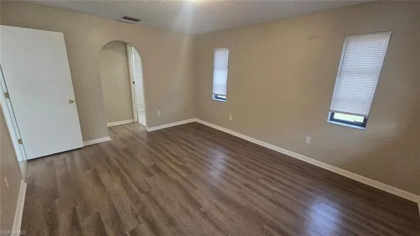 Spare room featuring arched walkways, a textured ceiling, and dark wood finished floors