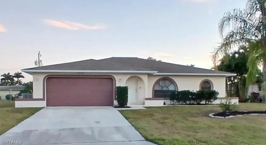View of front of house with stucco siding, driveway, and a yard