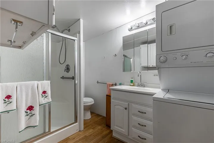 Bathroom featuring hardwood / wood-style flooring, stacked washer / dryer, vanity, toilet, and walk in shower