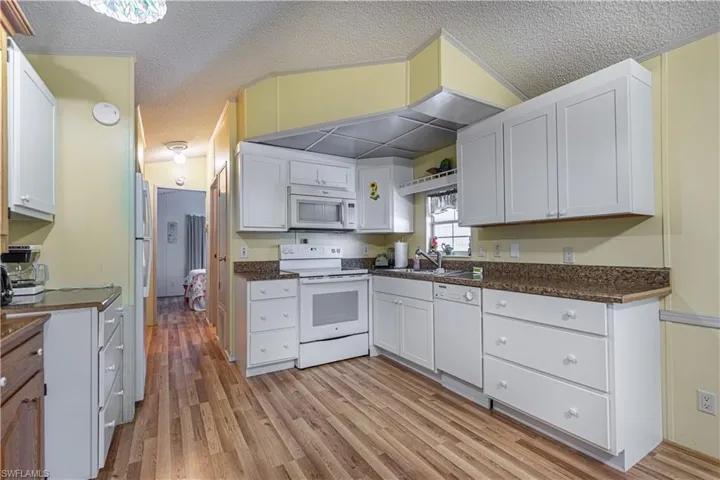 Kitchen with light wood-type flooring, white appliances, sink, and white cabinets