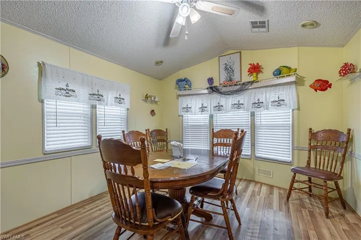 Dining area featuring wood-type flooring, lofted ceiling, a textured ceiling, and ceiling fan