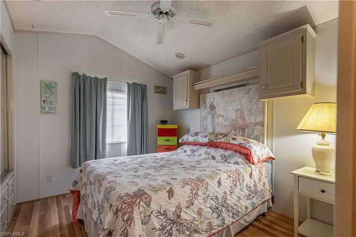 Bedroom with vaulted ceiling, wood-type flooring, ceiling fan, and a textured ceiling