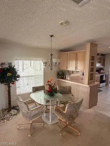 Dining room with light colored carpet, hanging lights, a textured ceiling, and light tile patterned flooring