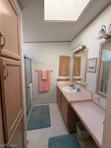 Bathroom featuring a shower stall, vanity, a skylight, light flooring, and crown molding
