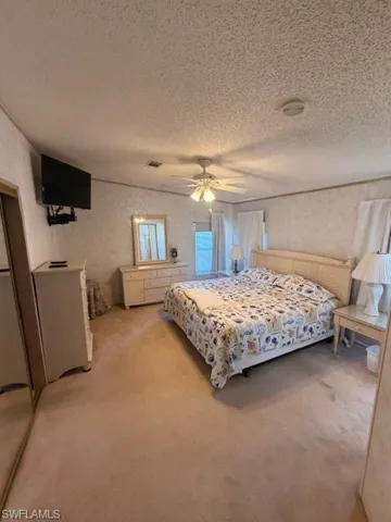 Carpeted bedroom with wallpapered walls, ceiling fan, and a textured ceiling