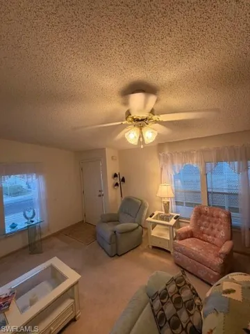 Living area with ceiling fan, carpet floors, and a textured ceiling