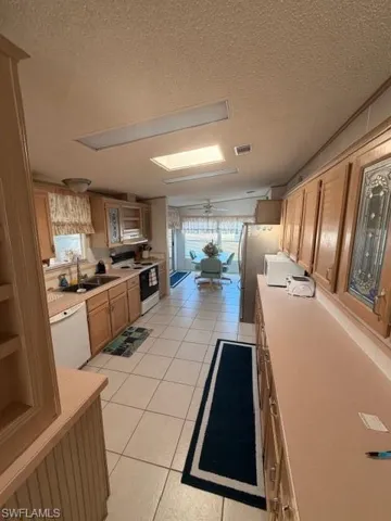Kitchen featuring a textured ceiling, light tile patterned floors, light countertops, stove, and dishwasher