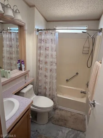 Bathroom with vanity, shower / bath combo with shower curtain, crown molding, and a textured ceiling