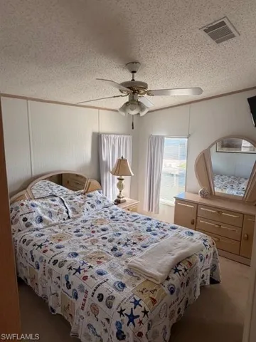 Bedroom with a textured ceiling, carpet flooring, crown molding, and a ceiling fan