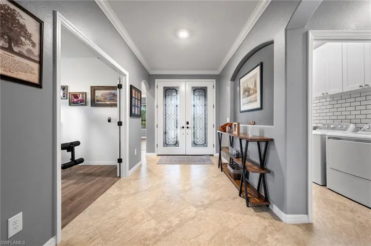 Double entry doors with decorative glass panels, tile flooring, crown molding, and an arched doorway