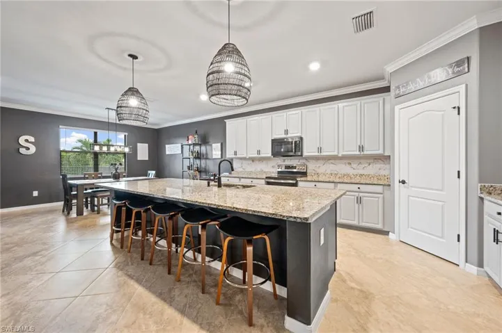 Kitchen featuring a large island with stone countertop, custom painted cabinetry with custom wrapped dark matching stainless steel appliances, and tile flooring