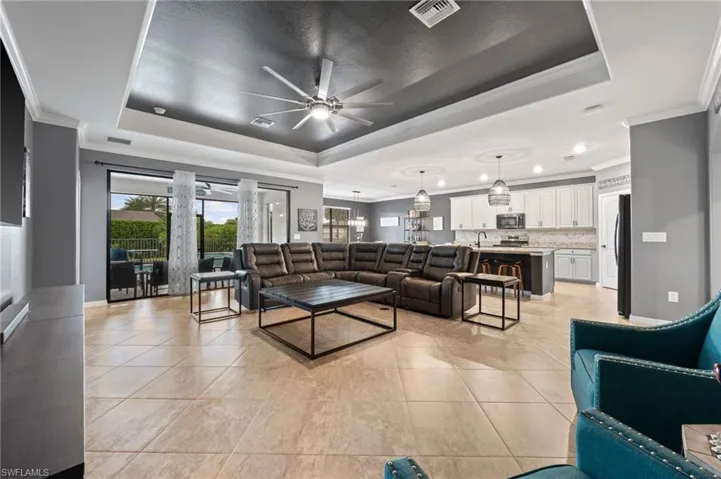 Tray ceiling with ceiling fan, large format tile flooring, sliding glass doors, custom painted cabinetry, and pendant lighting