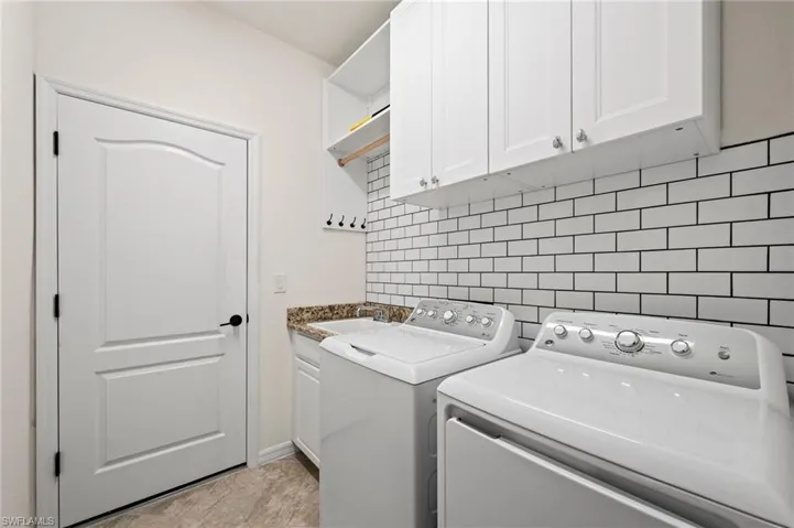 White subway tile backsplash, white shaker-style cabinetry, granite-finish countertop, light-toned flooring, and built-in shelving
