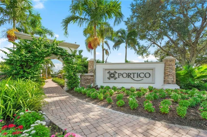 Portico community entrance sign with stone column accents, paver pathway, archway with climbing greenery, and mature palm trees