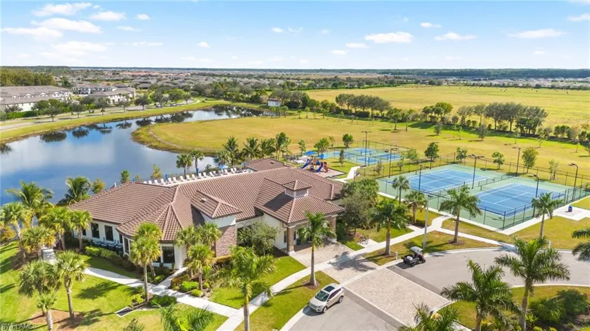 Community clubhouse with a barrel tile roof, surrounded by mature palm trees, featuring an adjacent tennis court, pickleball courts, and a playground