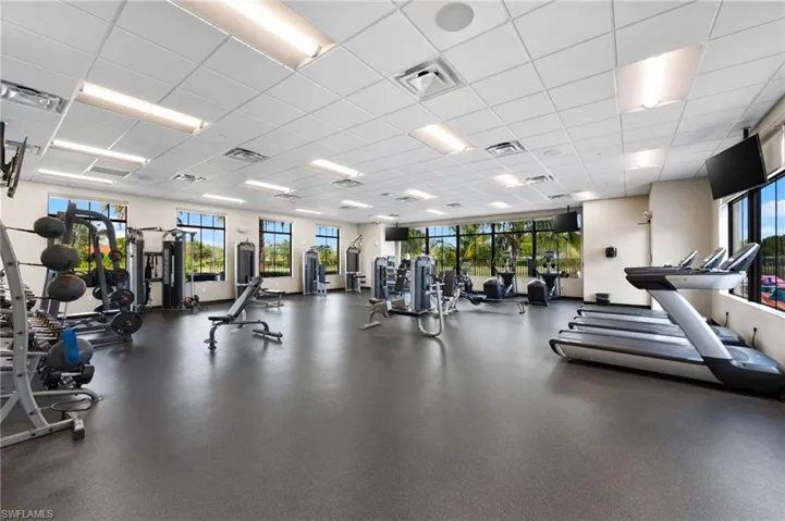 Expansive fitness center featuring rubberized flooring, abundant natural light from multiple windows, and a comprehensive selection of exercise equipment