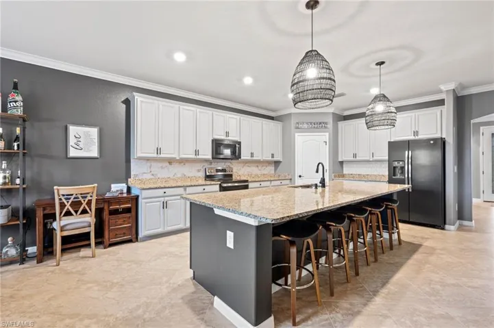 Spacious kitchen featuring two toned custom painted cabinetry, light-toned countertops, tile flooring, and a large central island with seating and recessed  lighting and Island Pendants