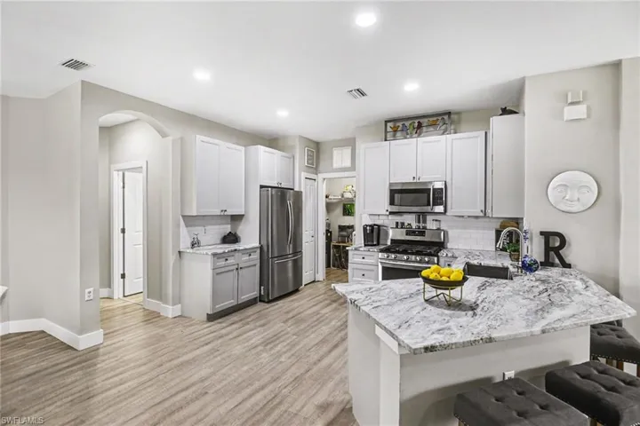 Bright kitchen featuring white cabinetry, stainless steel appliances, a white tile backsplash, and an island with a light-toned countertop