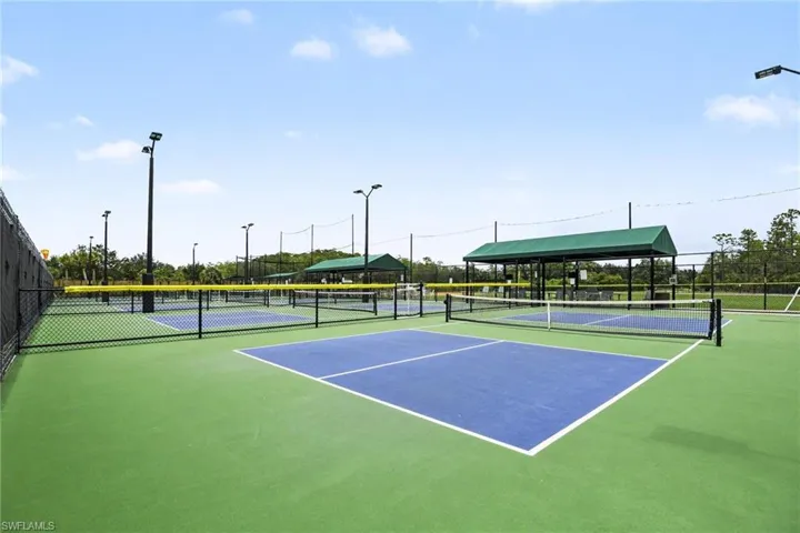 Multiple pickleball courts featuring green and blue surfacing, black chain-link fencing, and overhead lighting