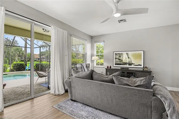 Living area featuring wood-finish flooring, a modern ceiling fan, and sliding glass doors opening to a screened patio with a pool