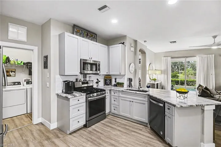 Modern kitchen featuring white shaker cabinetry, stainless steel appliances, a white subway tile backsplash, and light-toned wood-finish flooring