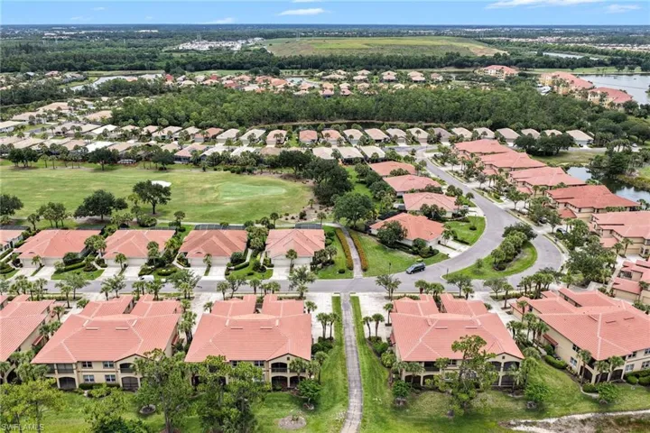 Aerial perspective showcasing a residential community with terracotta-style roofs, manicured golf course frontage, roadways, and mature landscaping