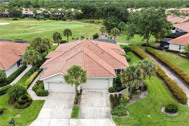 Residential property featuring a tile roof, two-car garage, concrete driveway, mature palm trees, and manicured landscaping