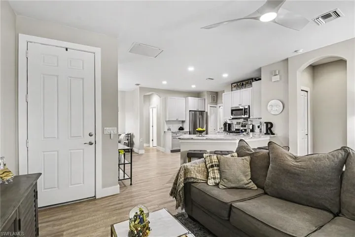 Open-concept living space featuring wood-finish flooring, a contemporary ceiling fan, recessed lighting, white kitchen cabinetry, and stainless steel appliances