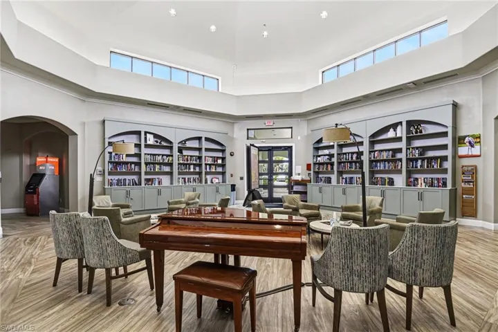 Spacious common area featuring a vaulted ceiling with clerestory windows, built-in shelving, wood-finish flooring, and a grand piano
