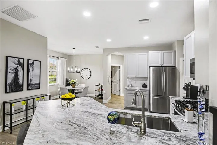 Spacious kitchen featuring a large island with a stone-finish countertop, stainless steel sink with gooseneck faucet, light-colored cabinetry, and stainless steel appliances