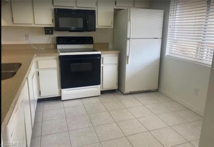 Kitchen with range with electric stovetop, freestanding refrigerator, black microwave, white cabinets, and light tile patterned floors