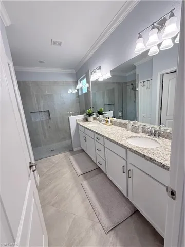 Full bathroom with a stall shower, double vanity, and ornamental molding