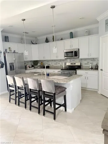 Kitchen with ornamental molding, decorative backsplash, a spacious island, white cabinets, and a breakfast bar