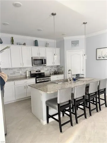 Kitchen with decorative backsplash, stainless steel appliances, a kitchen breakfast bar, an island with sink, and white cabinets