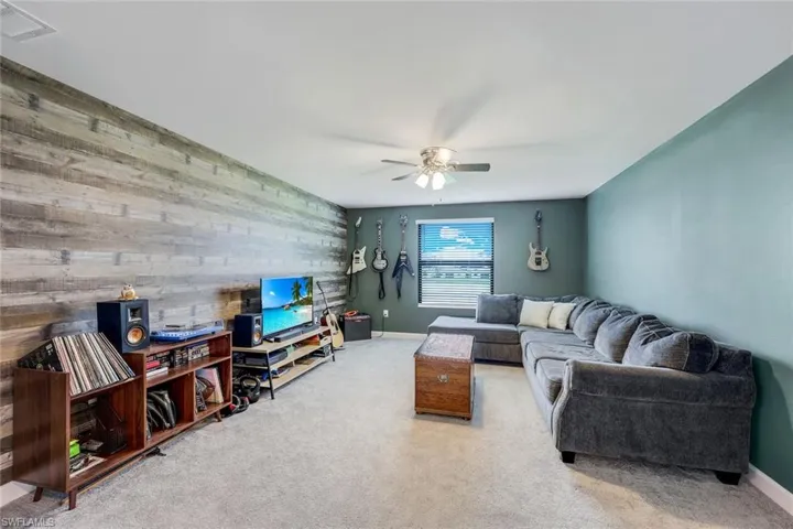 Living room featuring carpet flooring, wood walls, and ceiling fan