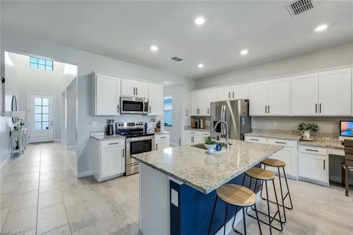 Kitchen featuring light stone countertops, appliances with stainless steel finishes, a kitchen island with sink, white cabinets, and a breakfast bar area