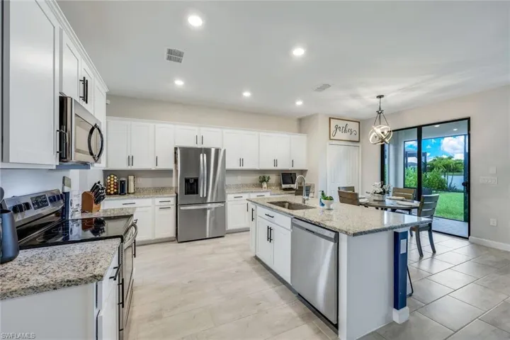 Kitchen with appliances with stainless steel finishes, white cabinetry, sink, and a center island with sink