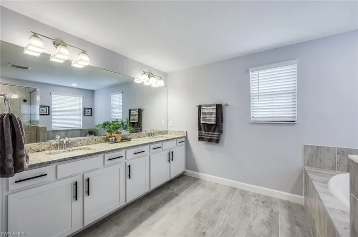 Bathroom featuring a relaxing tiled bath, plenty of natural light, oversized vanity, and dual sinks