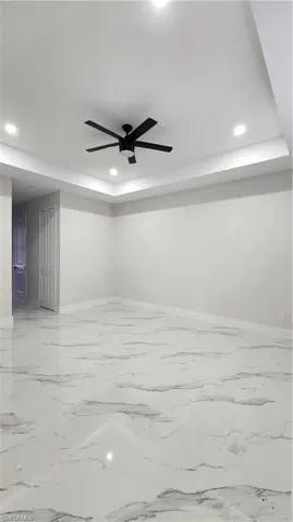 Primary room with a tray ceiling, recessed lighting, a ceiling fan, and light marble finish floors