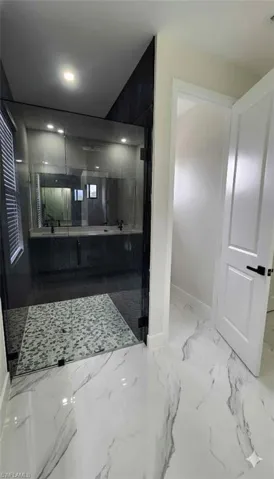 Full bath featuring marble tiled floors, a marble finish shower, and double vanity